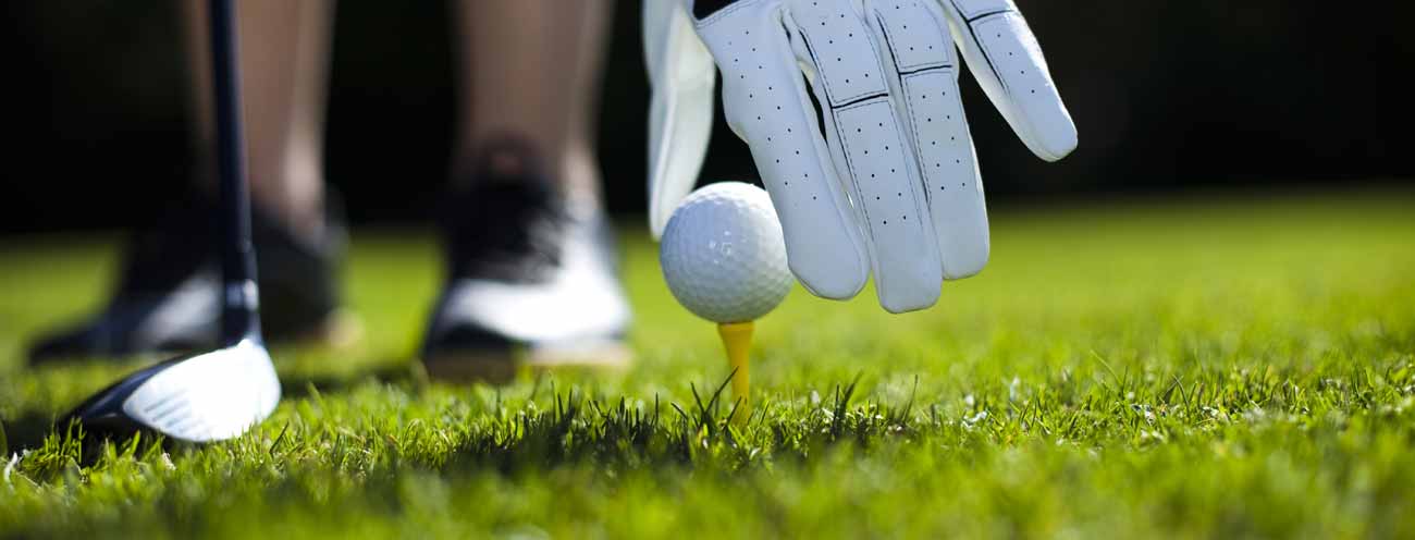 A Hand with golf glove sets a golf ball off the grass